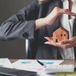 Female house insurance broker with a house model in her hand. House protection.